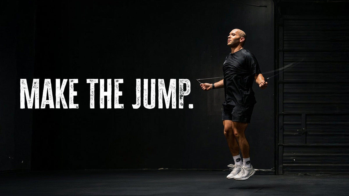 A man in a black athletic outfit and white sneakers jumps rope on a dark stage, with the text 'MAKE THE JUMP.' displayed on the left.