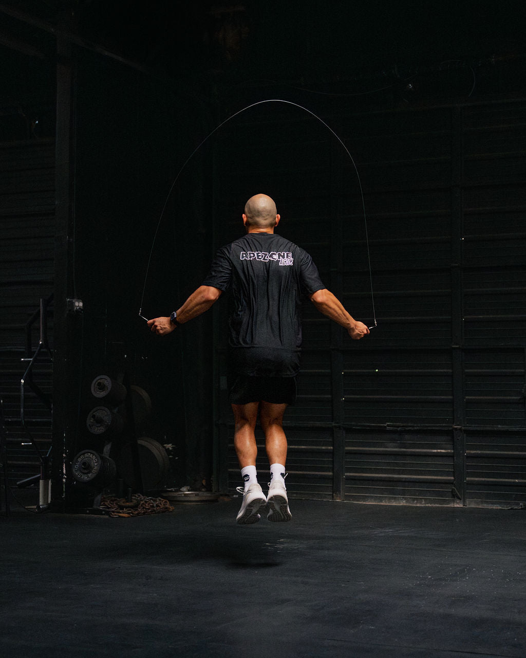 Person jumping rope in a dark indoor setting with a black wall.