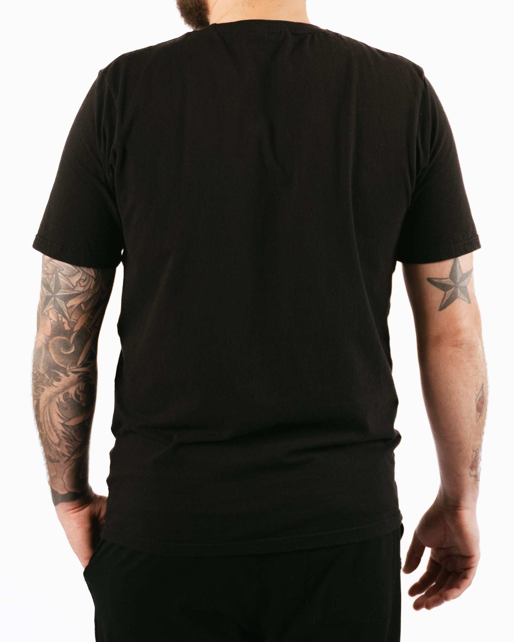 Person wearing a black t-shirt with visible tattoos on arms