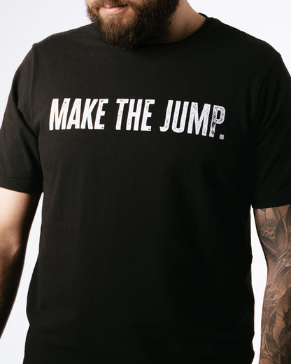 Black t-shirt with 'MAKE THE JUMP.' text worn by a person with tattoos on a white background