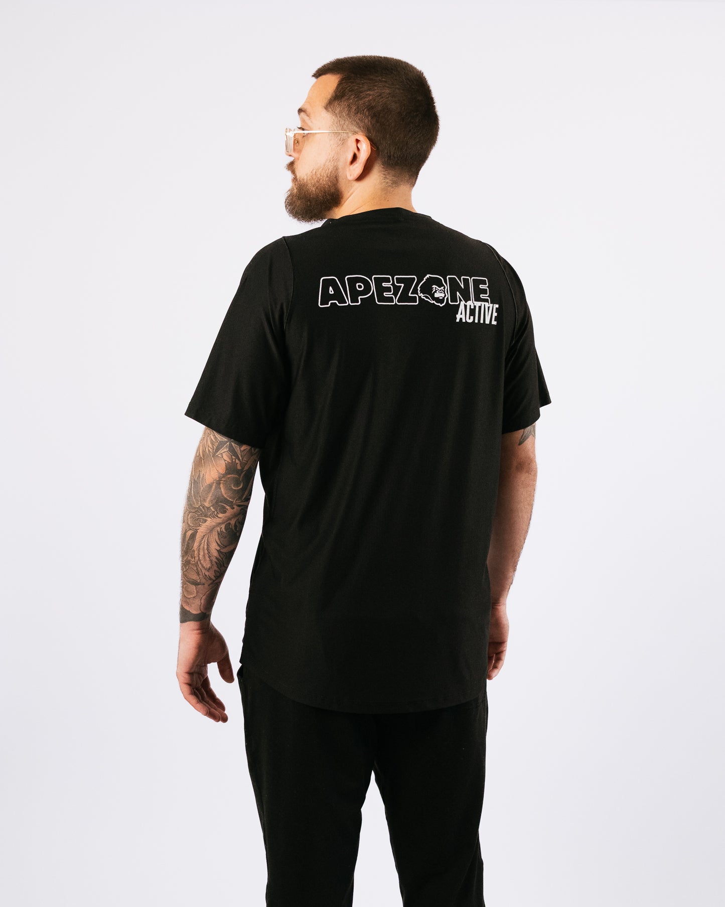 Man wearing a black t-shirt with 'APEZONE ACTIVE' text on the back, standing against a white background