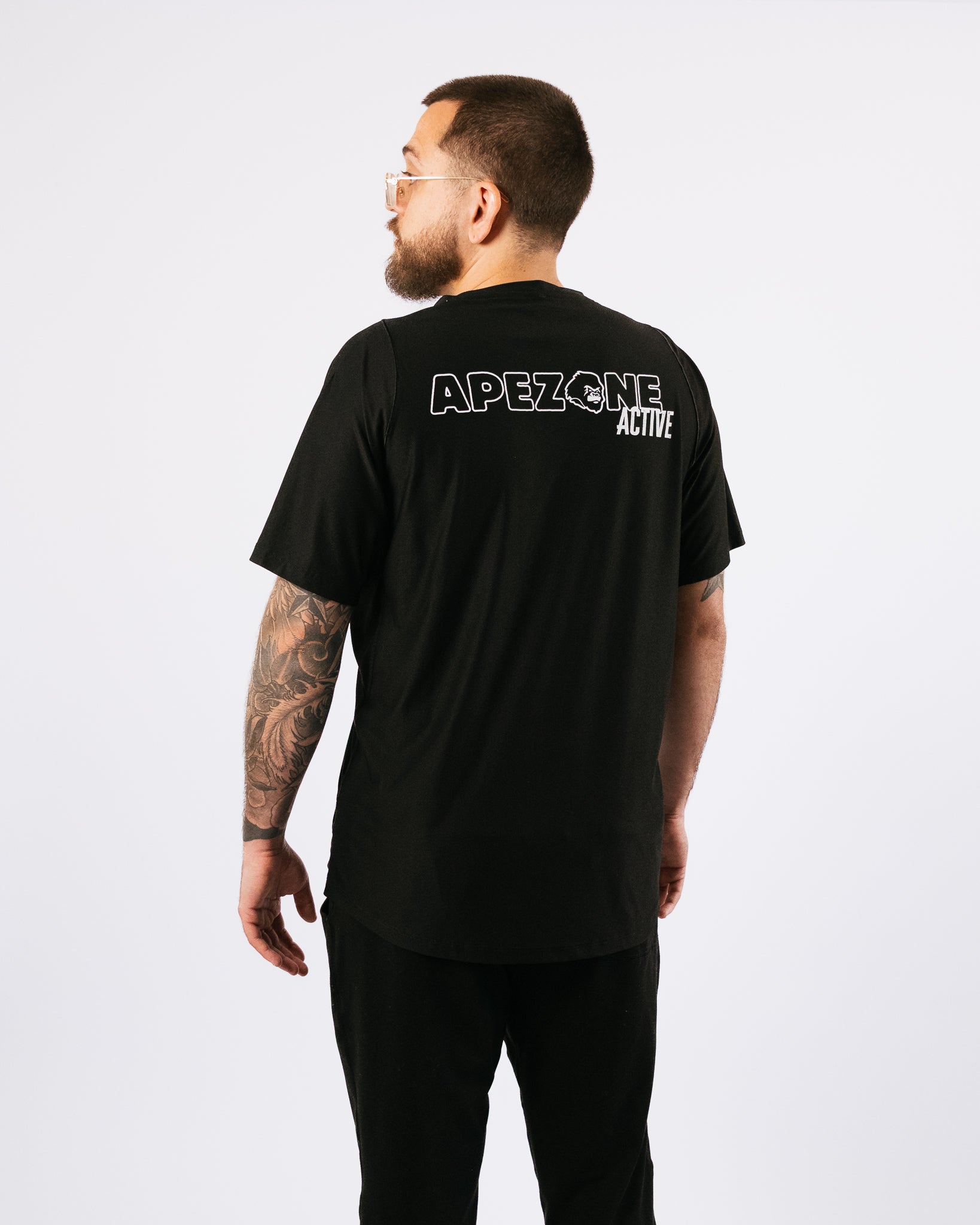Man wearing a black t-shirt with 'APEZONE ACTIVE' text on the back, standing against a white background