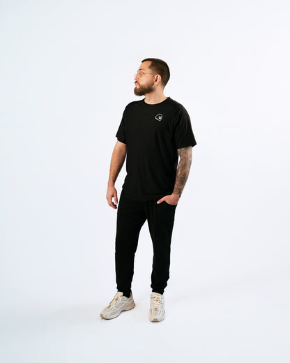 Man wearing a black t-shirt with a gorilla logo and pants on a white background